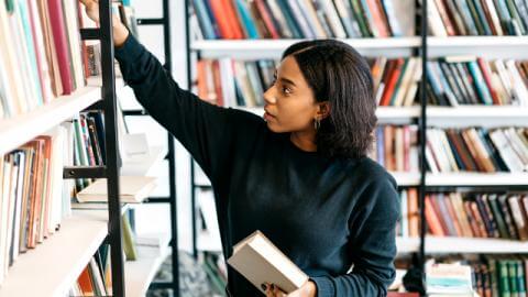 Young lady pulling books of bookshelf